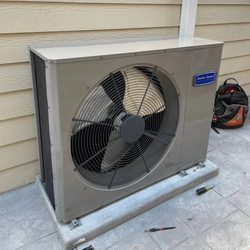 An outdoor HVAC unit sitting on a concrete pad next to a beige-siding wall.